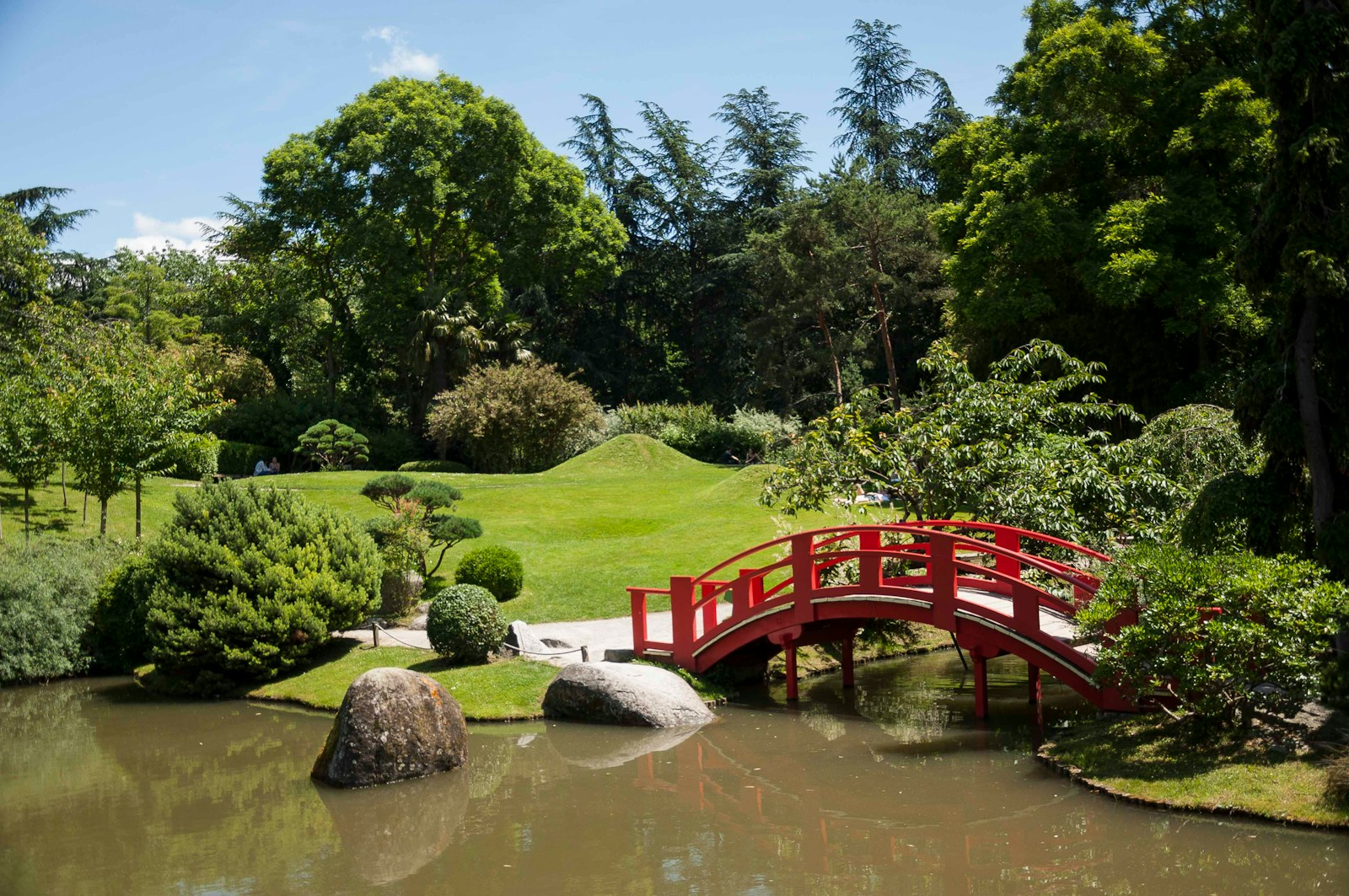 a red bridge over a small pond in a park